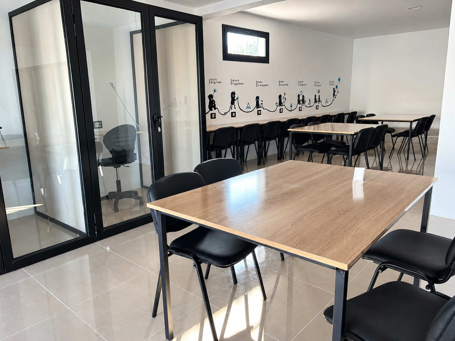Open coworking area with shared tables next to a row of glass workspaces